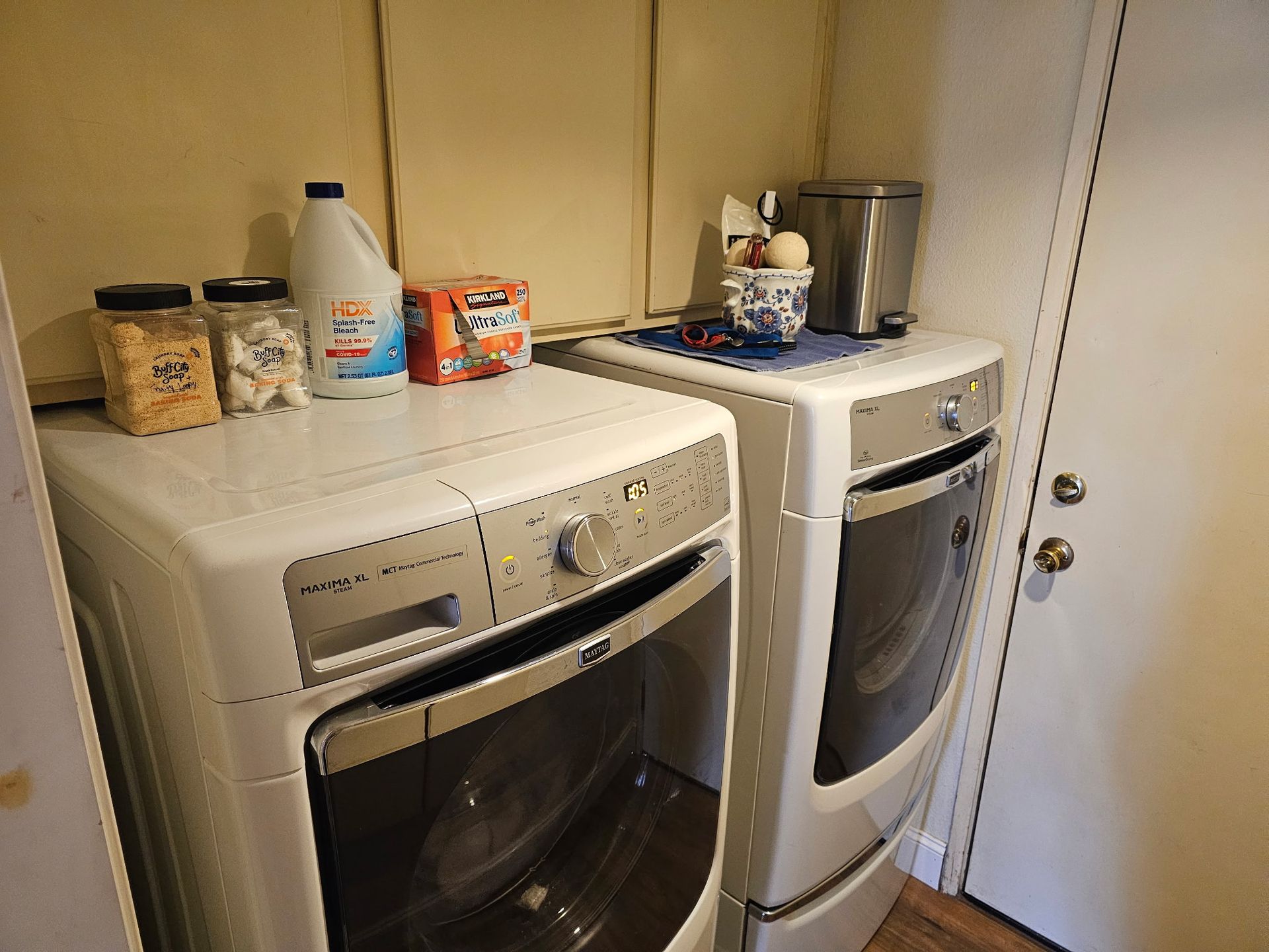 Laundry appliances with cleaning supplies on top, next to a door.
