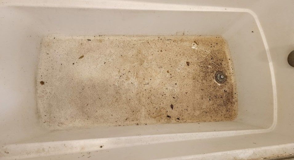 Dirty white bathtub with brown stains and debris in the bottom.