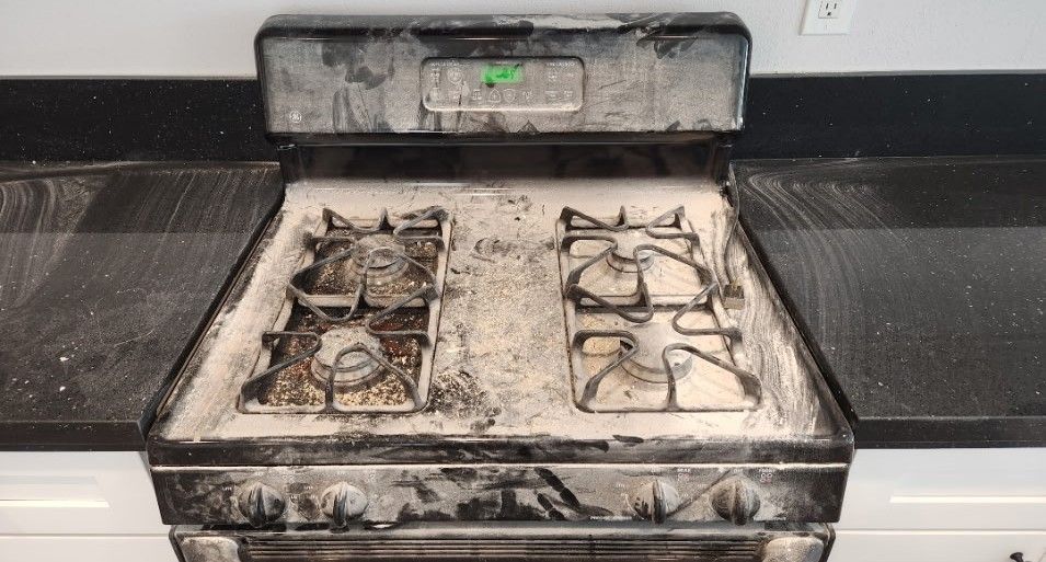 Dirty gas stove with heavy residue on the burners and cooktop, set against a dark countertop.