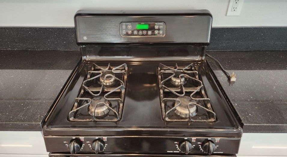 Black gas stove top with four burners and digital clock on the back.