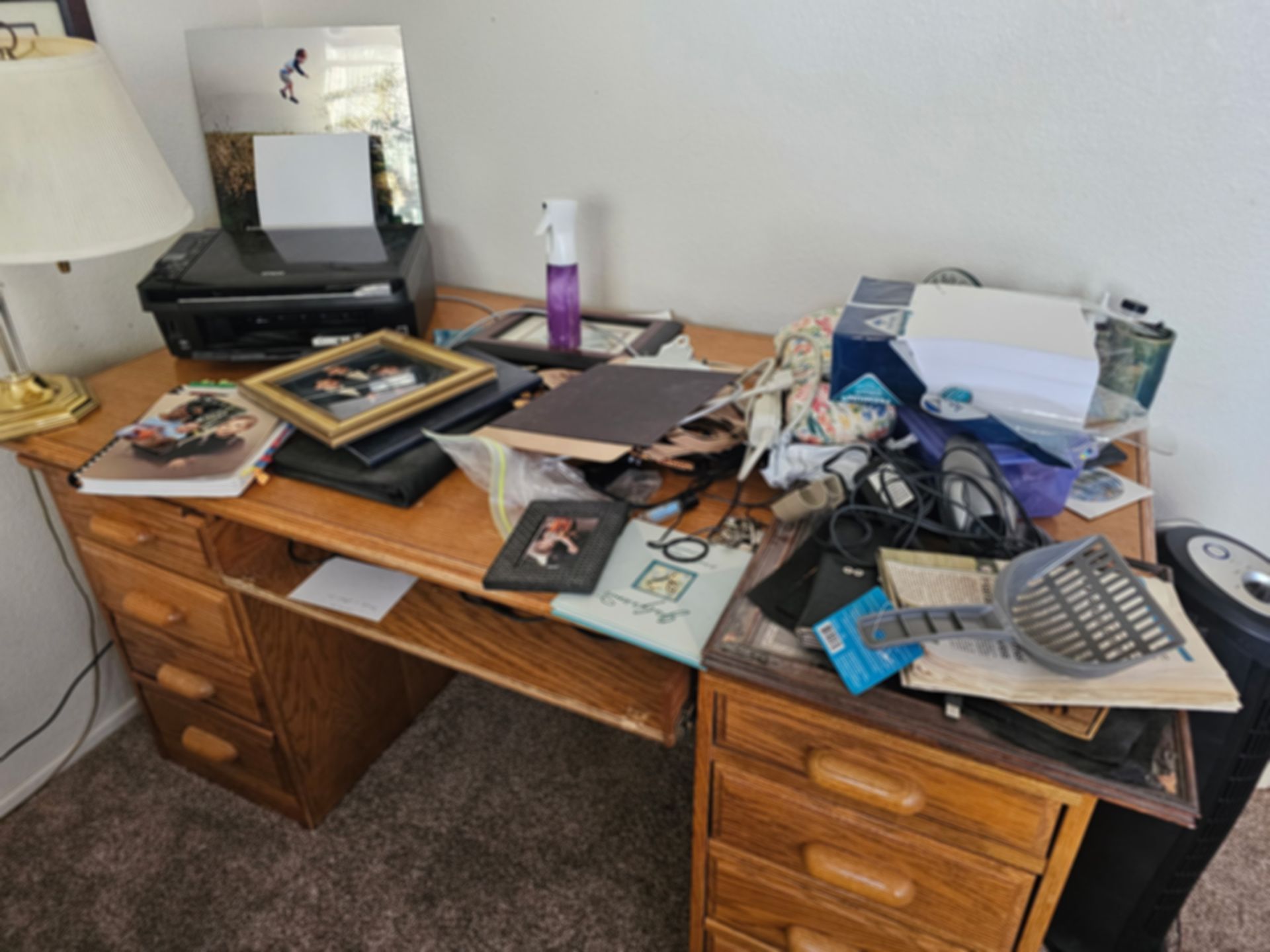 Wooden desk cluttered with various items including a printer, photos, and papers.