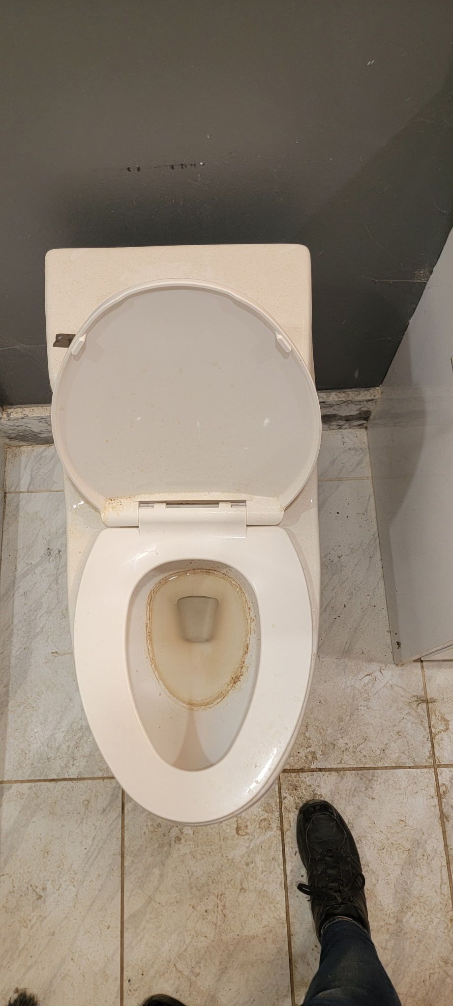 An overhead view of a dirty toilet, with the lid up, is in a tiled bathroom.