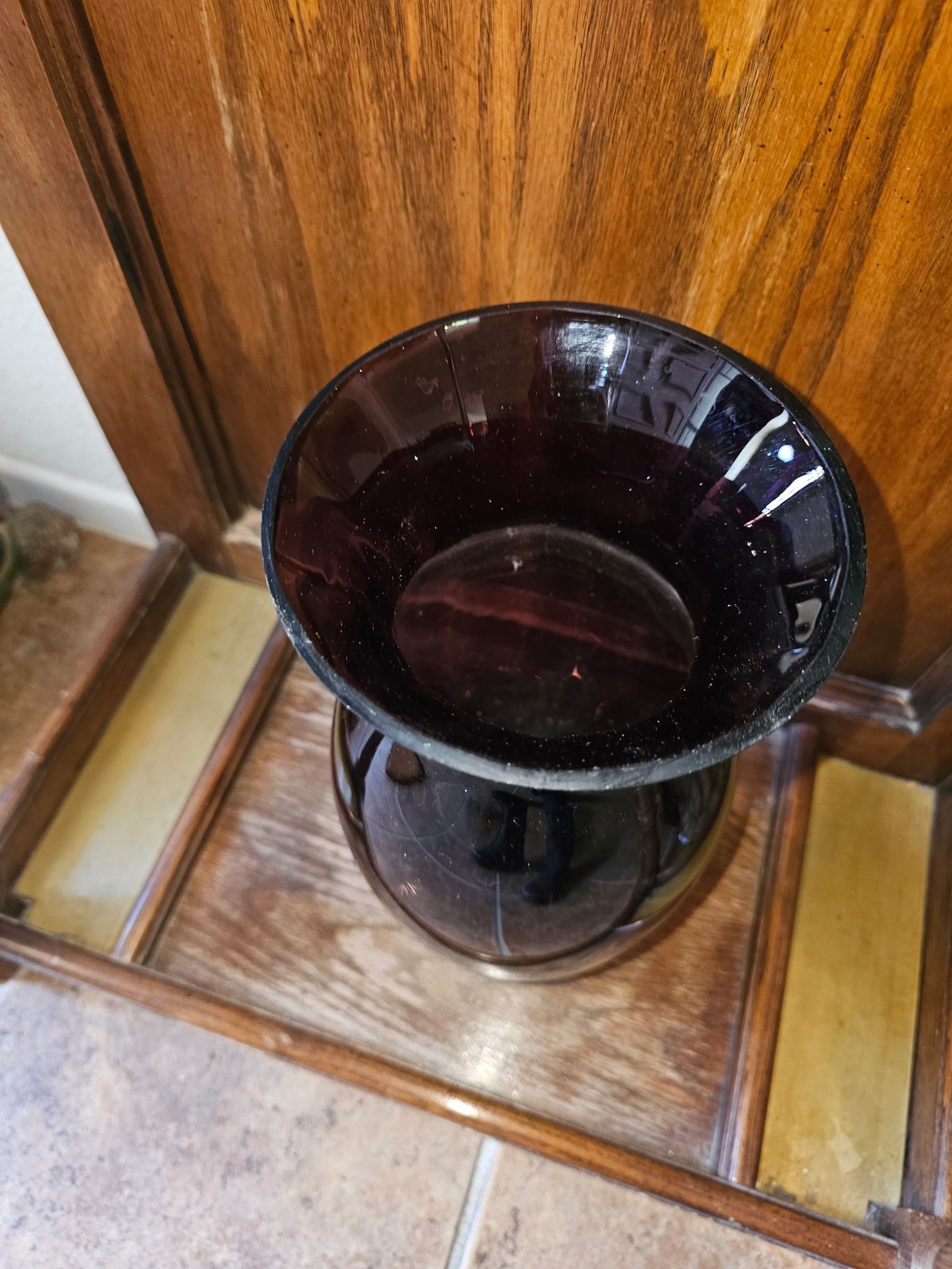 Dark purple glass vase with wide rim on wooden surface.
