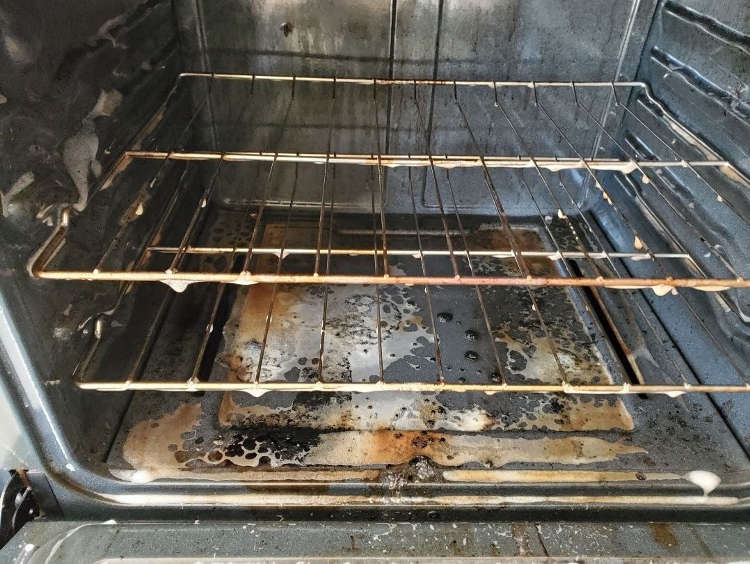 Dirty oven interior with racks and baked-on food residue, coated with cleaning solution.
