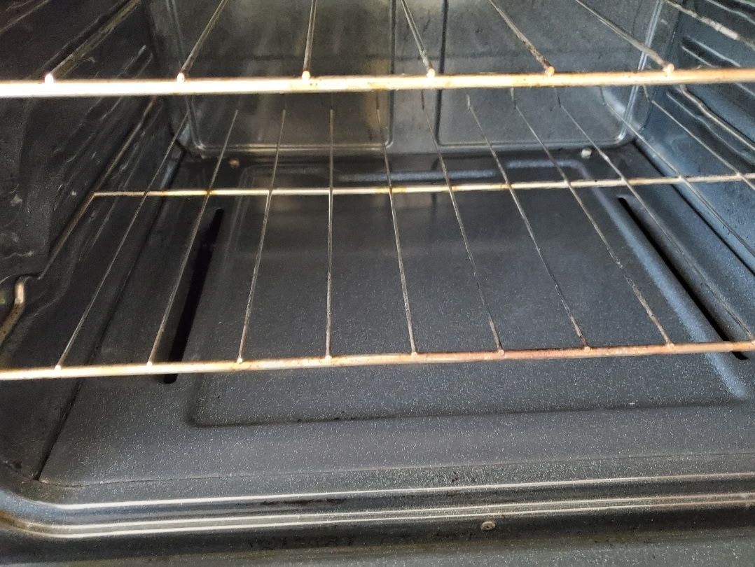 Interior of a dirty oven with two racks visible, showing food residue and stains on the oven floor.