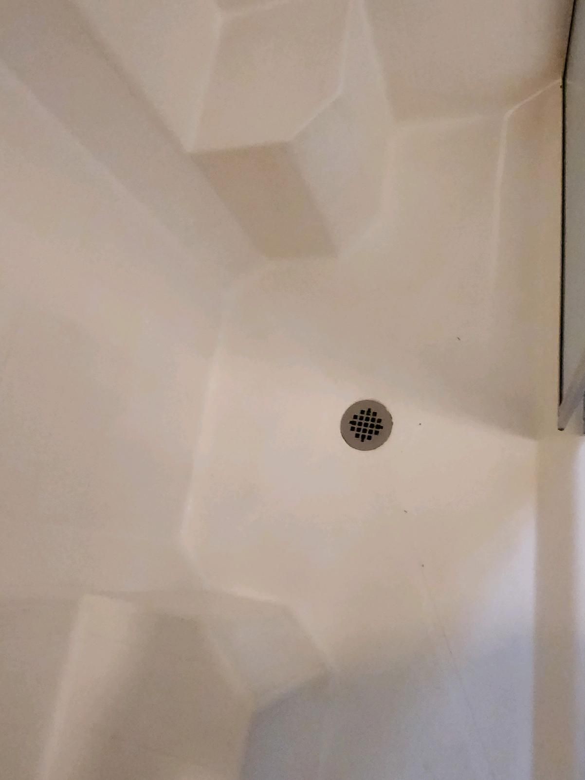 White shower stall with a drain in the center. The walls have angular shapes.