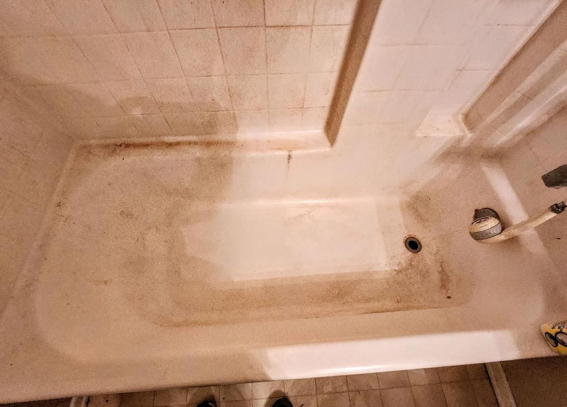 Dirty bathtub with brown stains and mildew. Tiles and a shower rod are visible.
