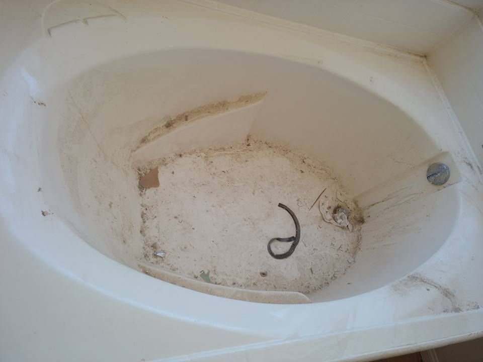 Dirty, oval-shaped bathtub. The bottom has stains and debris. A drain and overflow pipe are visible.