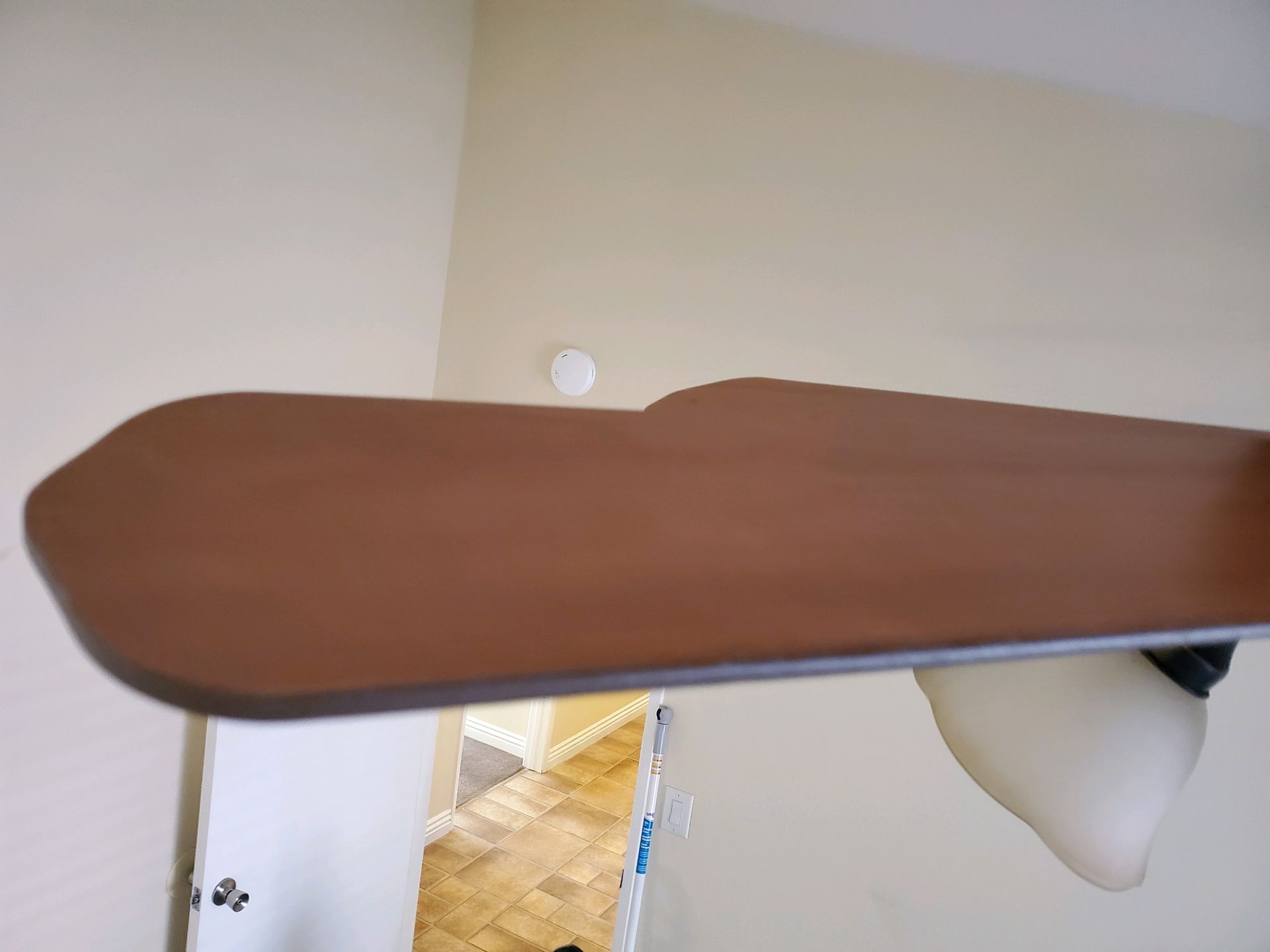 Ceiling fan blade, brown, with white light fixture, mounted on cream-colored wall.