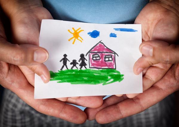 A person is holding a drawing of a family and a house A person is holding a drawing of a family and a house