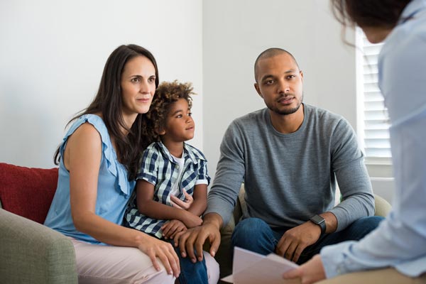 A family is sitting on a couch talking to a woman. A family is sitting on a couch talking to a woman.