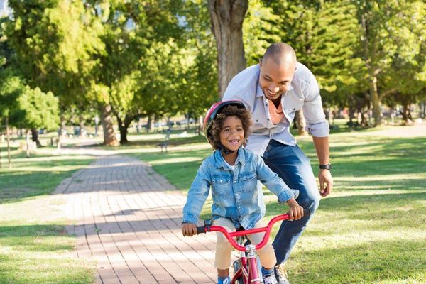 A man is teaching a little girl how to ride a bike in a park. A man is teaching a little girl how to ride a bike in a park.