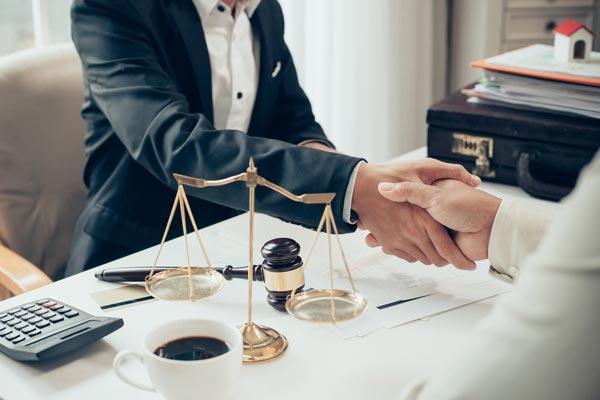 A man and a woman are shaking hands at a table with scales of justice. A man and a woman are shaking hands at a table with scales of justice.