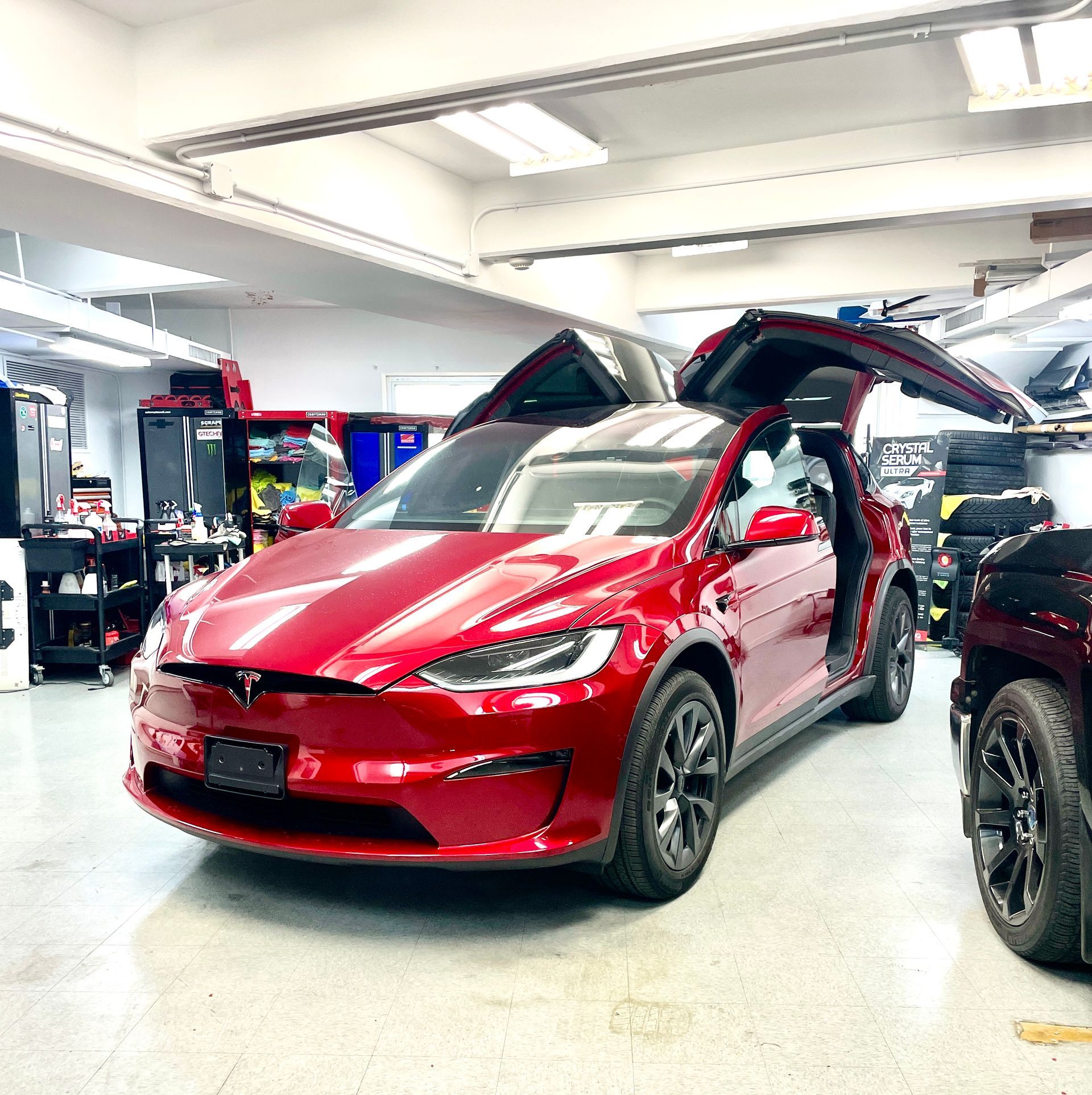 A red tesla model x is parked in a garage with its doors open.