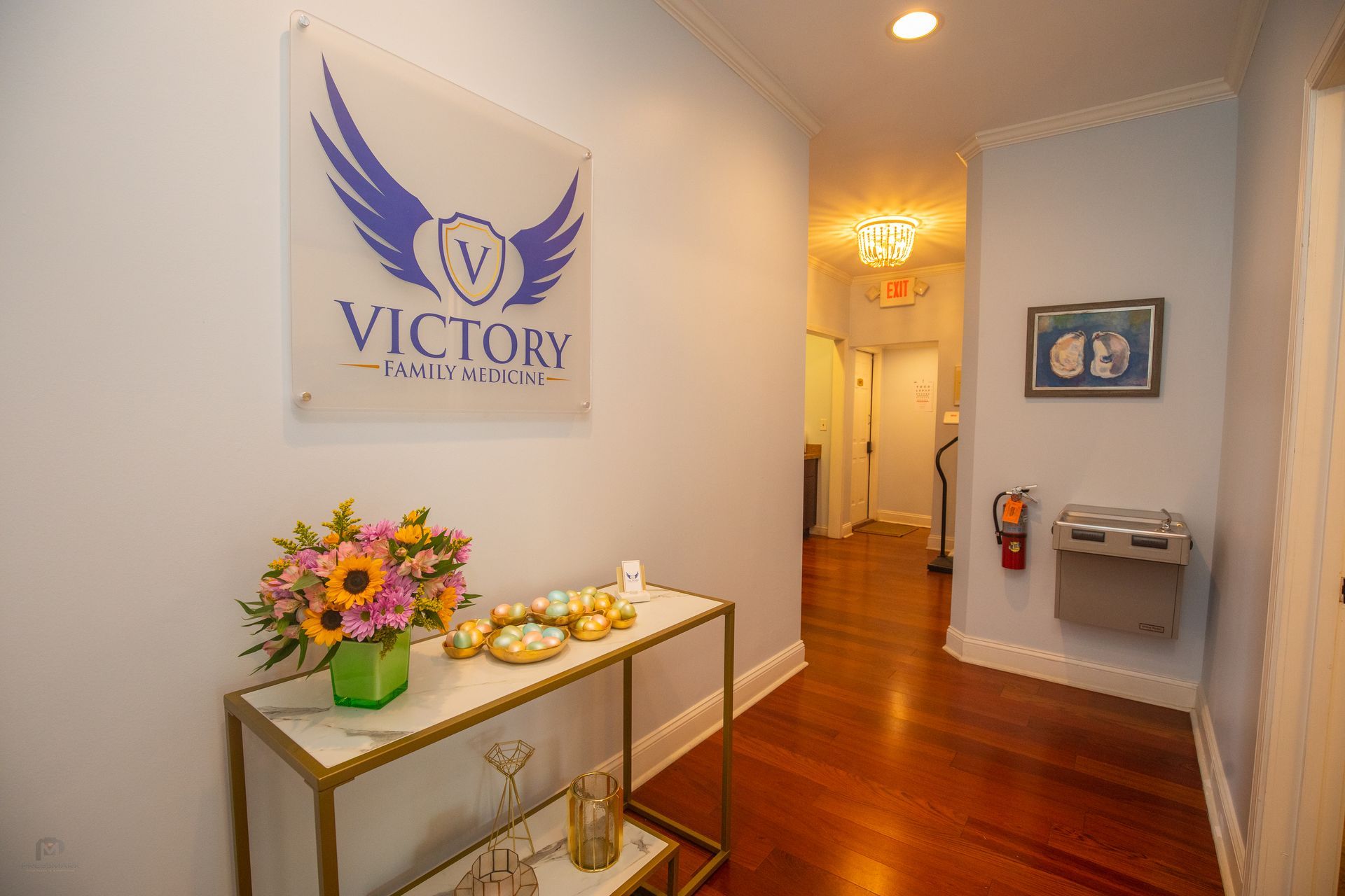 Hallway with Victory Health logo, flowers, and a fire extinguisher.