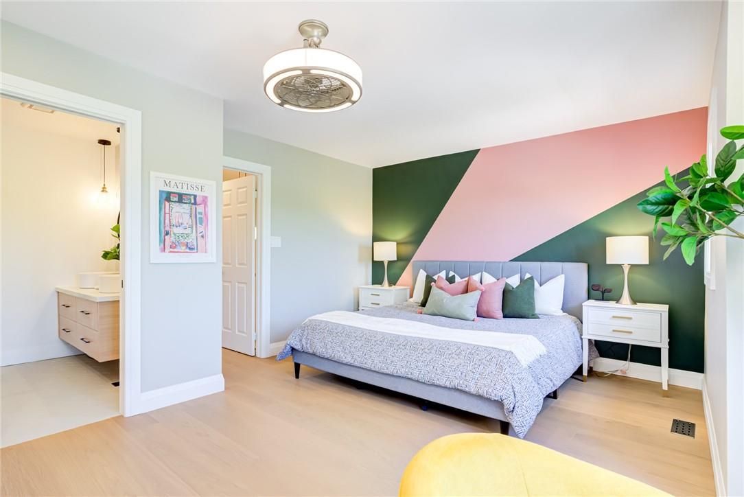Modern bedroom with a geometric pink and green accent wall behind a grey bed and white nightstands.