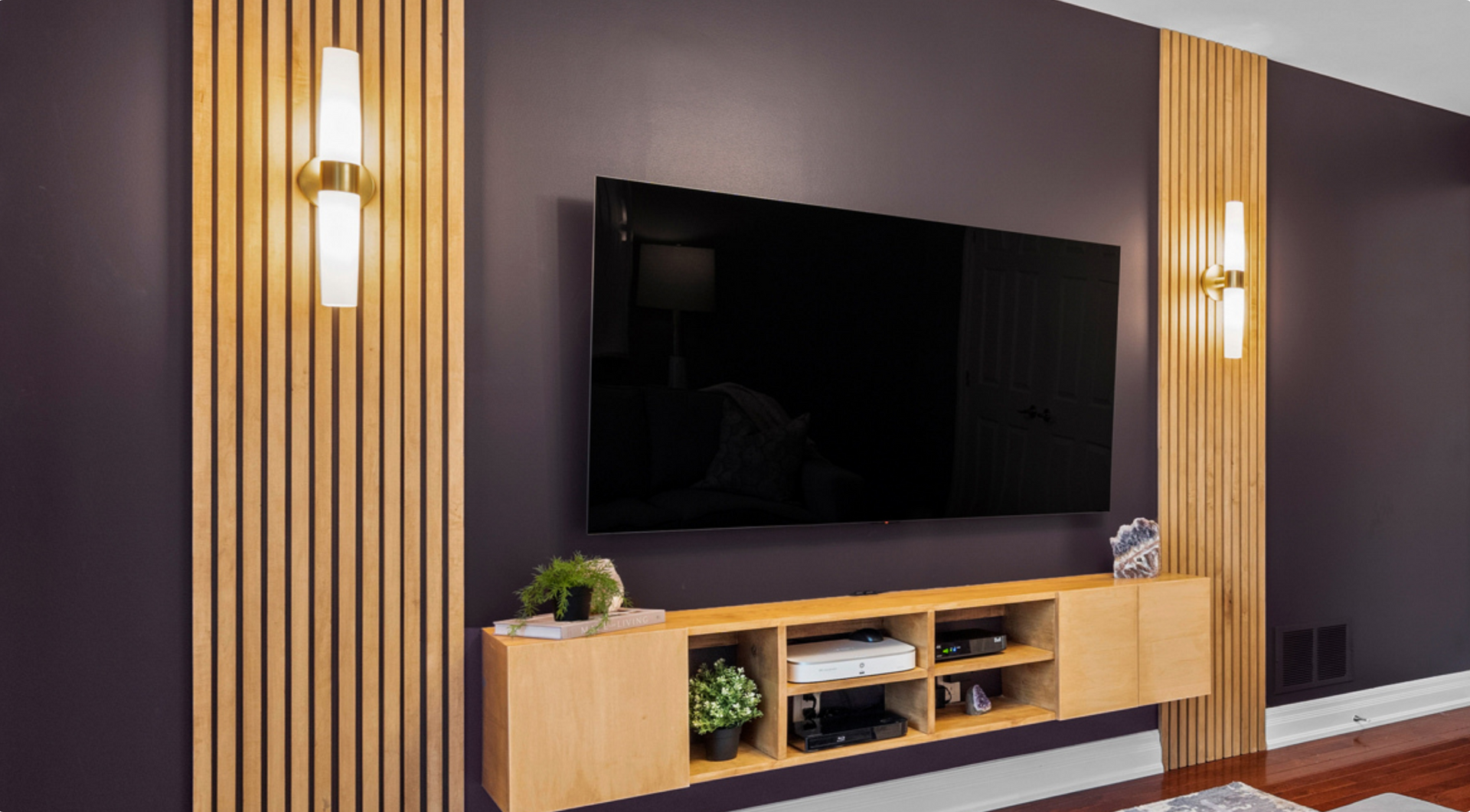 Wall-mounted TV centered between vertical wood slats and soft lighting, with a floating console below that adds visual balance and enhances interior calm.