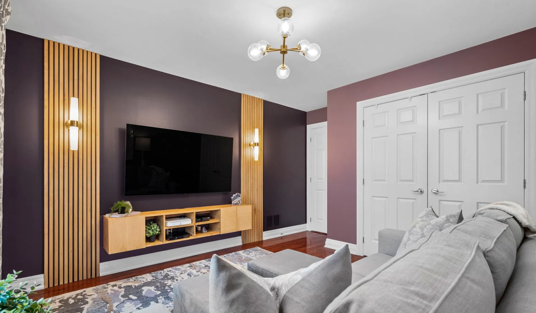 Modern living room with purple accent wall, mounted TV, wooden slat panels, floating media console, and gray sofa.