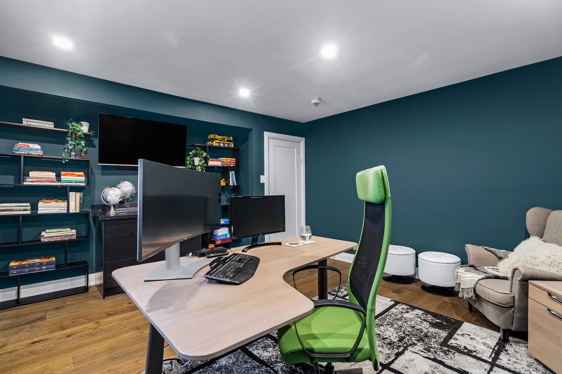 Modern home office with dual monitors, green accent chair, and dark blue walls.