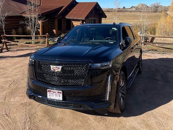 A black cadillac escalade is parked in front of a log cabin.