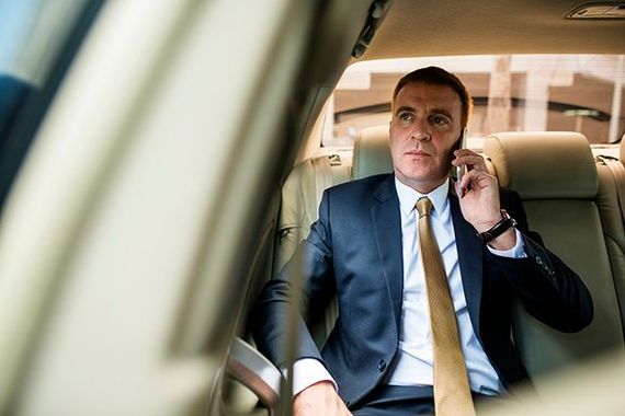 A man in a suit and tie is sitting in the back seat of a car talking on a cell phone.