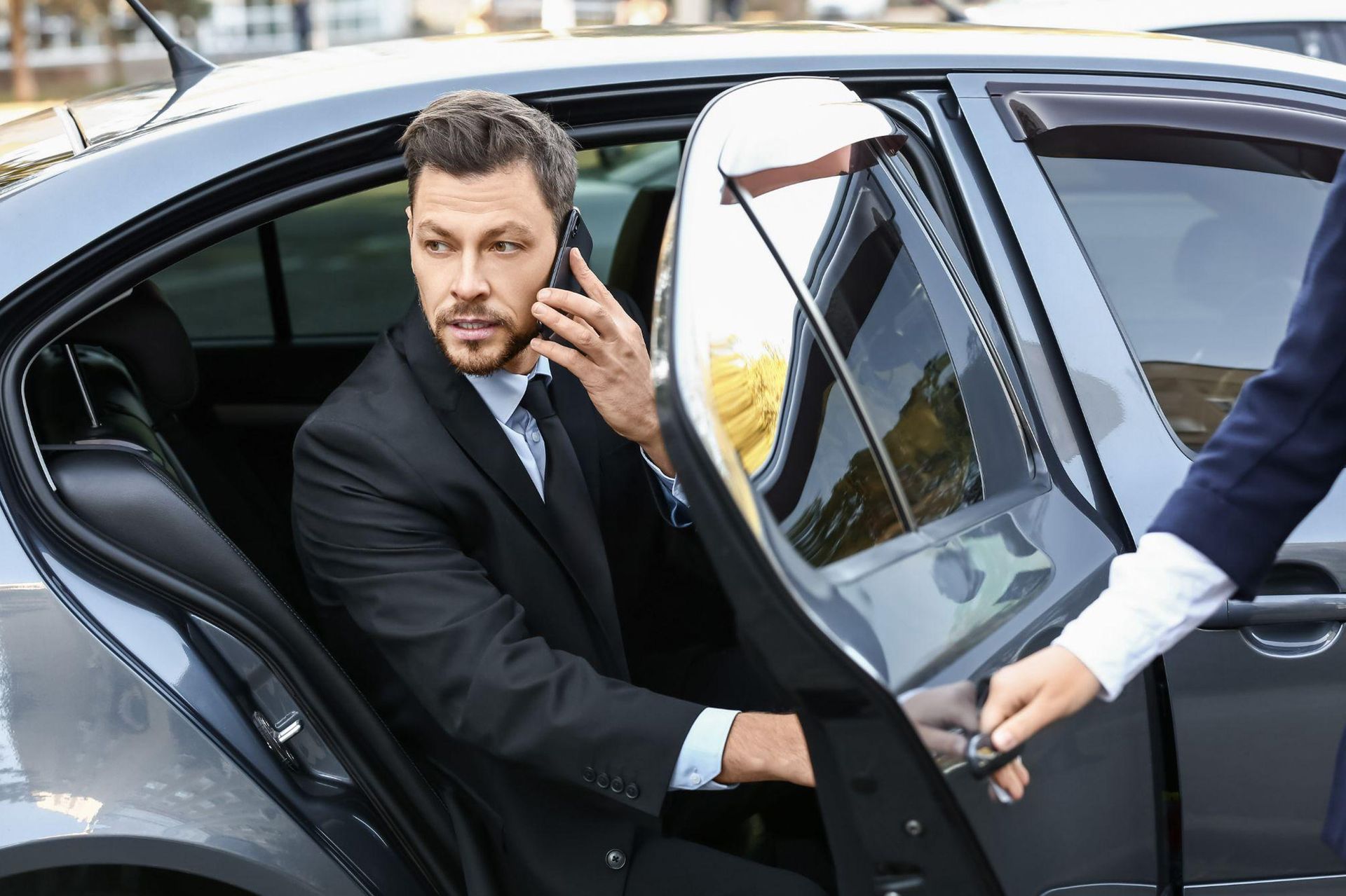 A man in a suit is getting out of a car while talking on a cell phone.