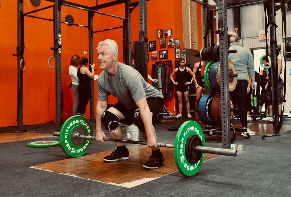 A man is squatting down to lift a barbell in a gym.