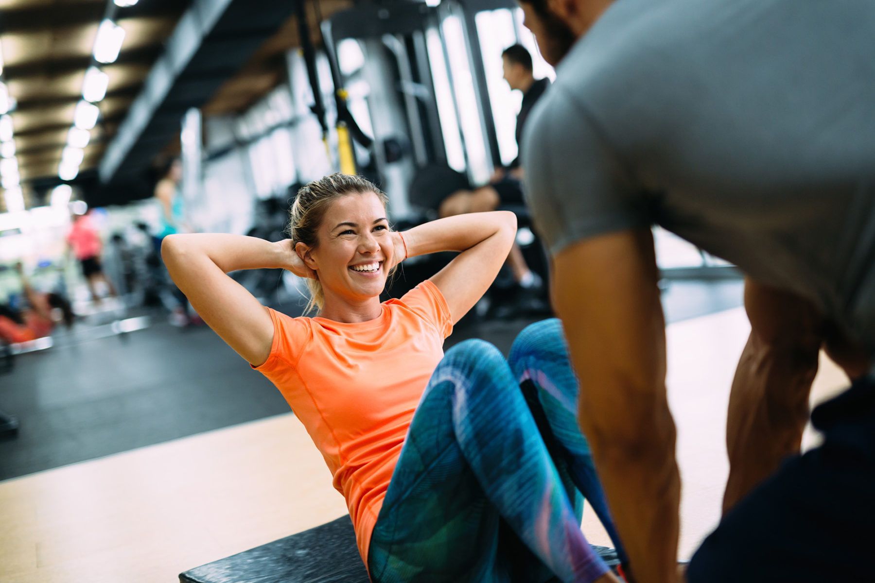 A man is helping a woman do sit ups in a gym.