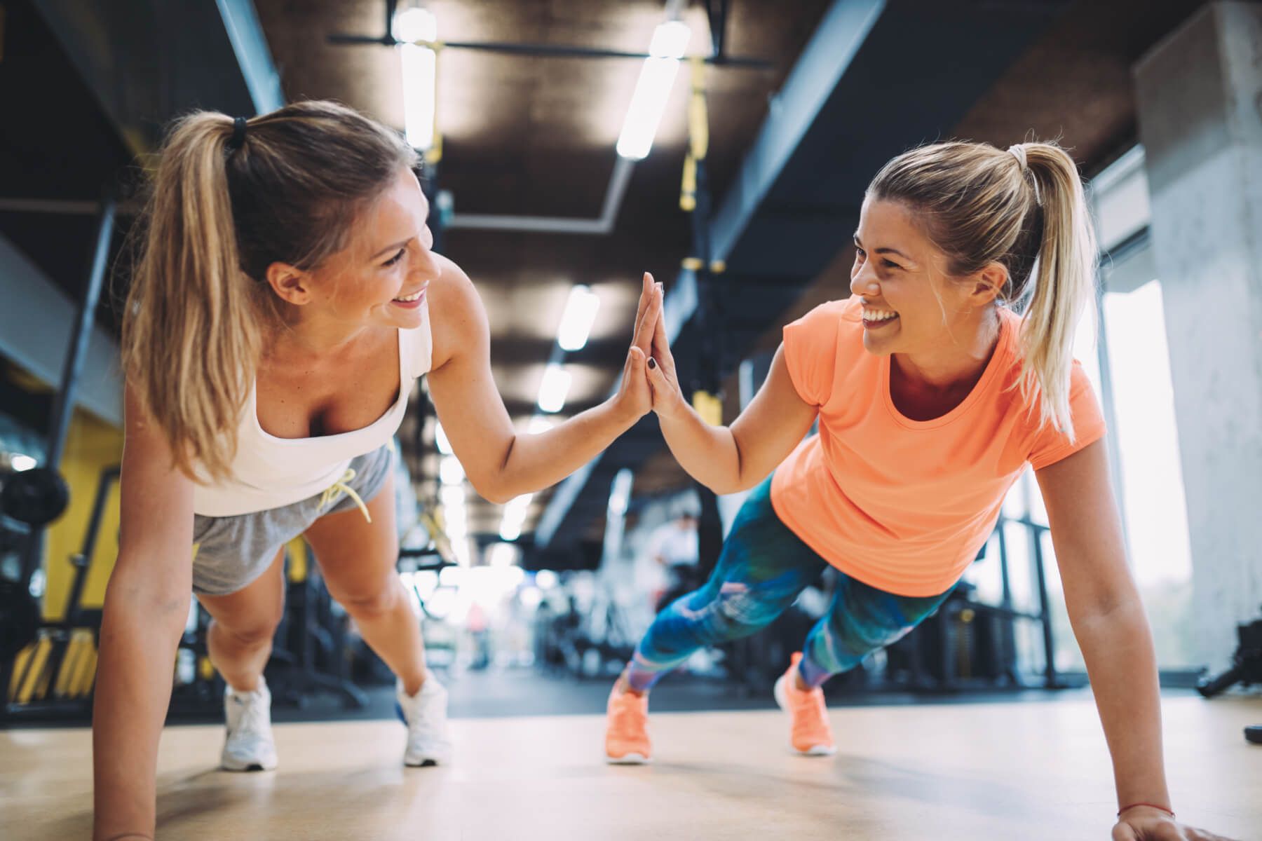 Two women are doing push ups in a gym and giving each other a high five.