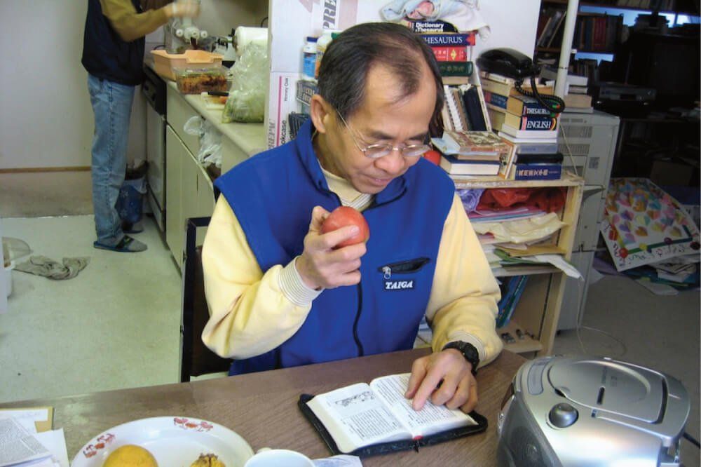 A man sitting at a table reading a book and eating an apple