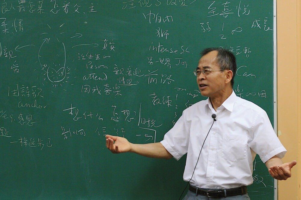 A man is giving a lecture in front of a green board