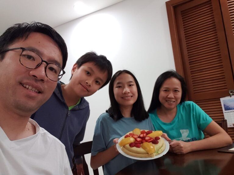 A man and three children are sitting at a table holding a plate of fruit