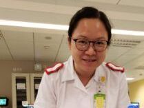 A nurse wearing glasses and a white uniform is smiling for the camera.