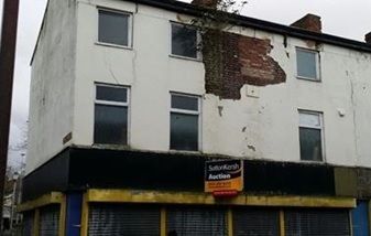 一棟白色建築,磚牆破損,上面掛著「拍賣」的牌子。