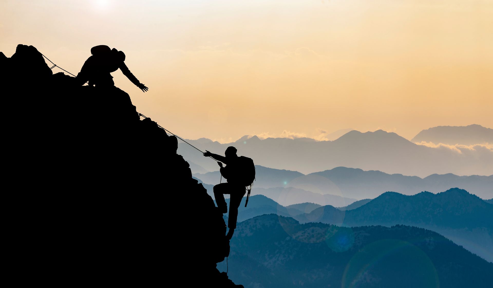 Silhouettes of two people climbing up a mountain