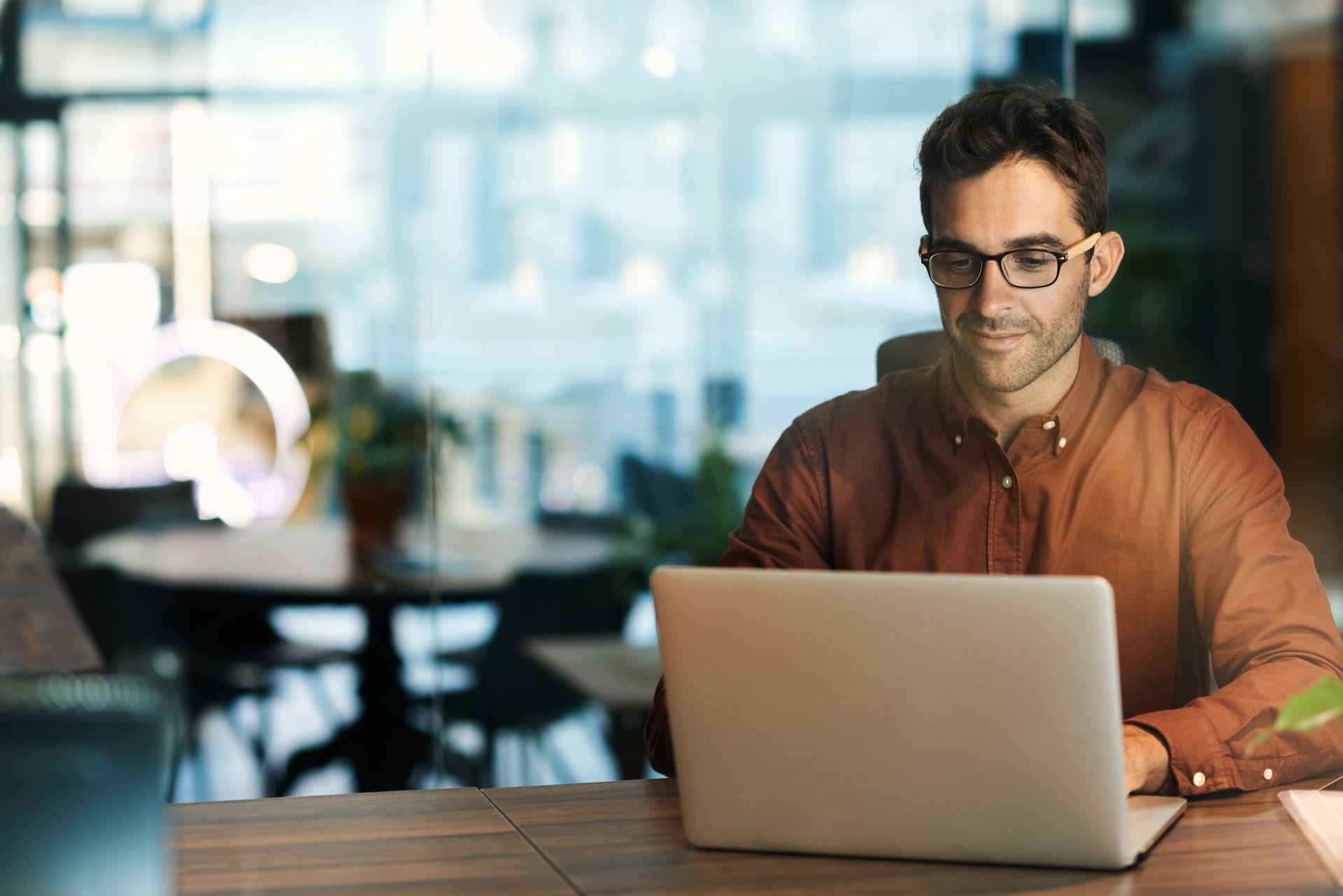 Man with glasses working on a laptop in a shared working space