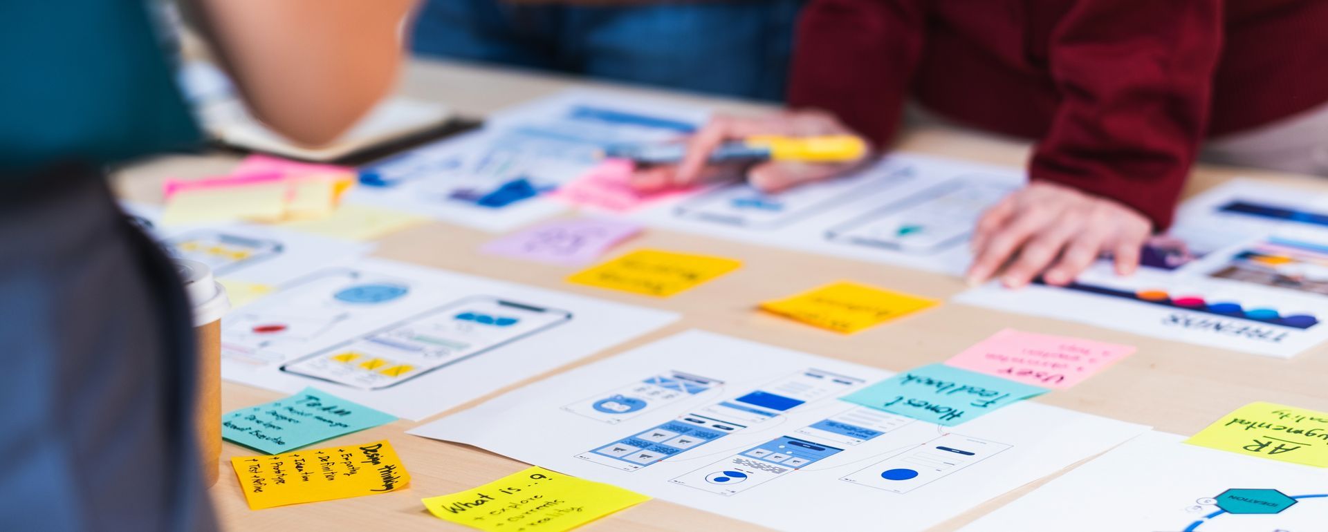 People working on a table with papers, sticky notes, and a marker.