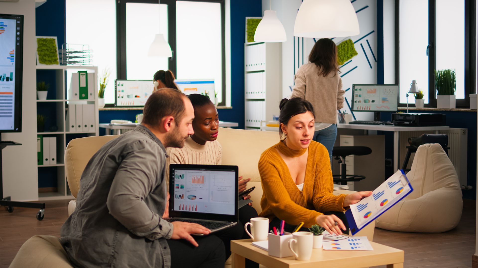 Three marketing professionals sitting together with a laptop and clipboard, reviewing digital market