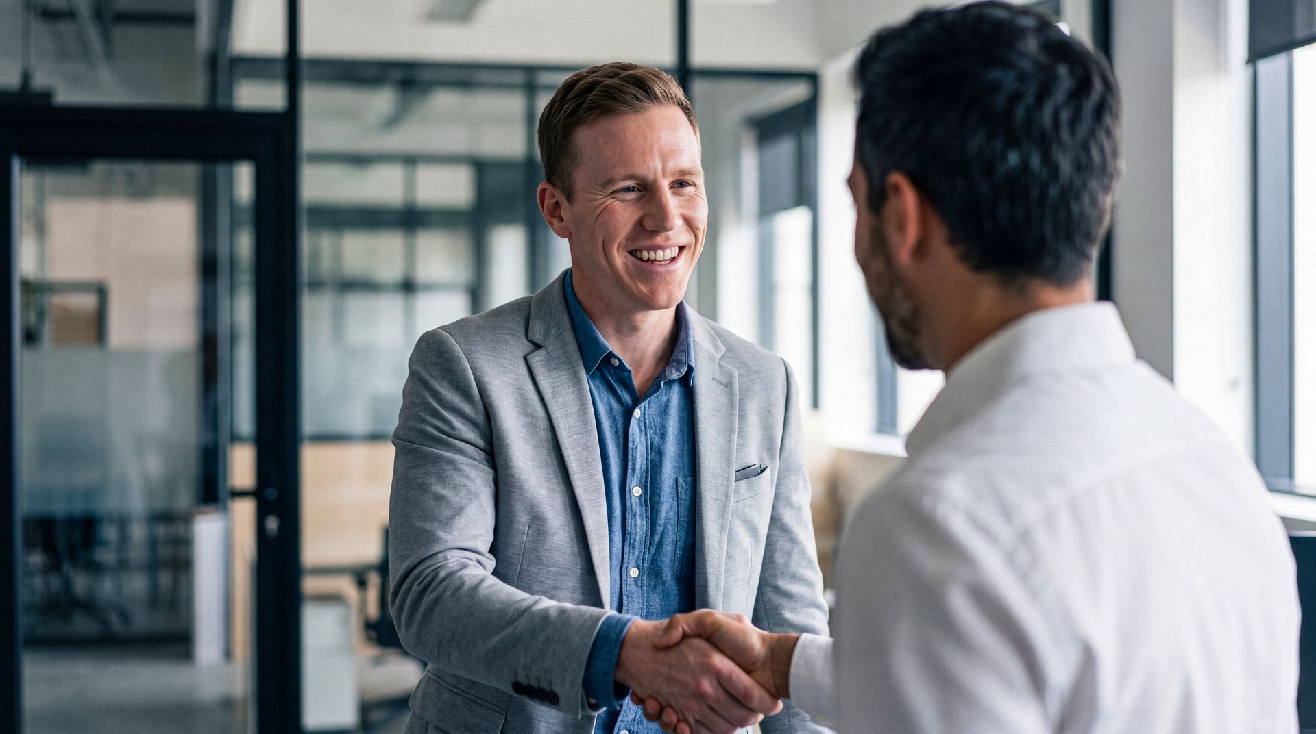 Smiling young businessman shaking hands with a client in a modern office setting