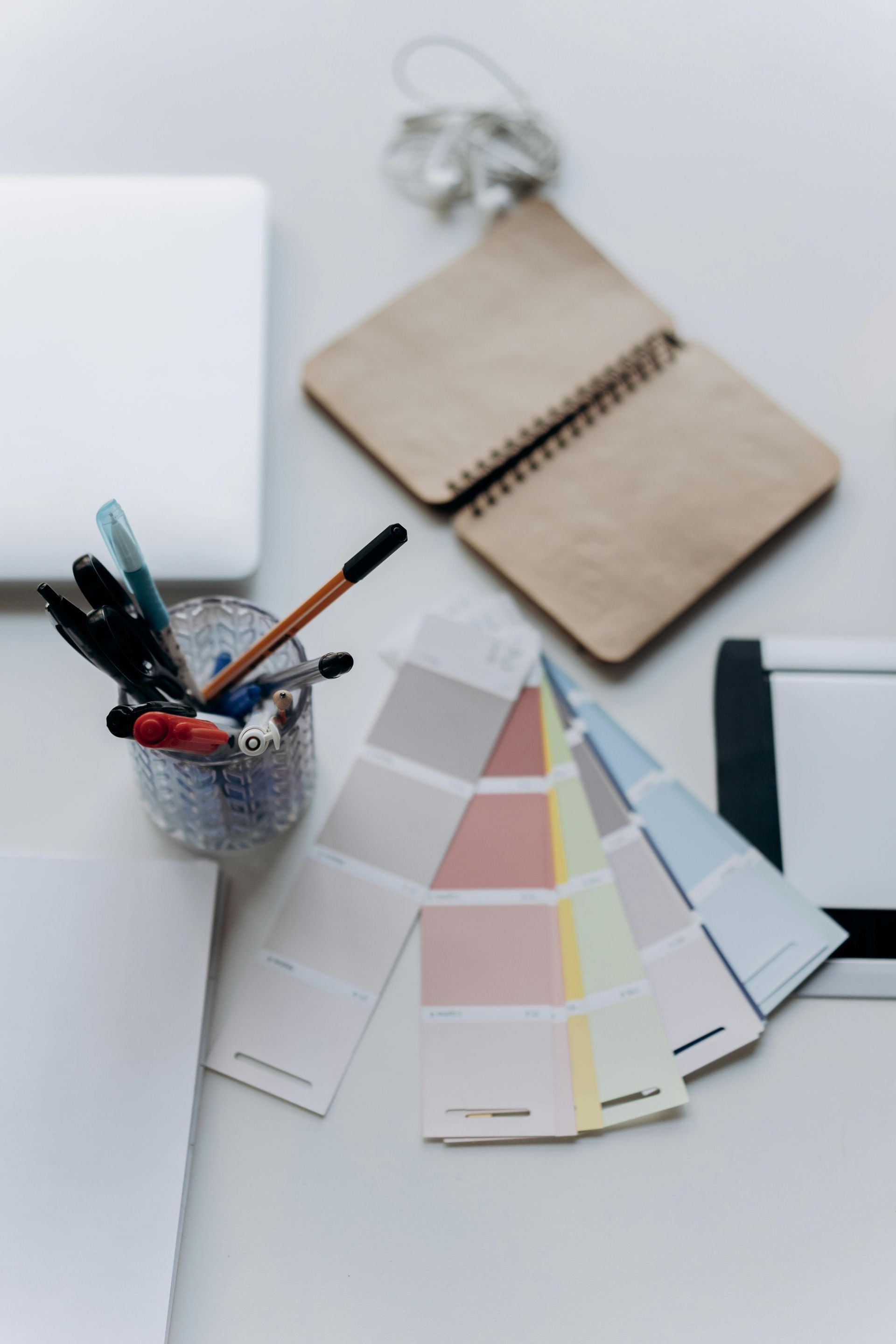 Workspace with color swatches, notebook, pens, and a laptop, suggesting design or creative work.