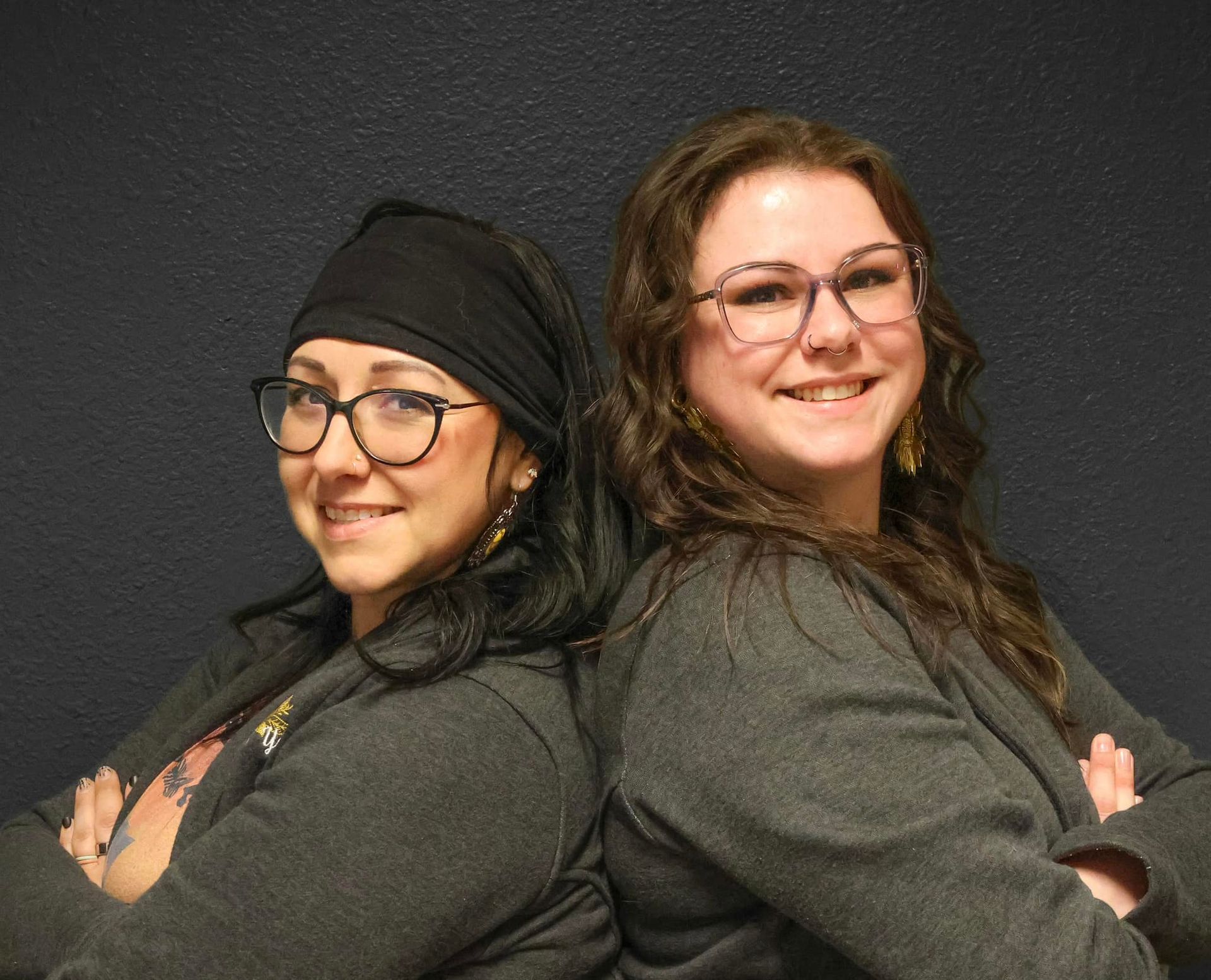 Two women are standing back to back with their arms crossed and smiling.