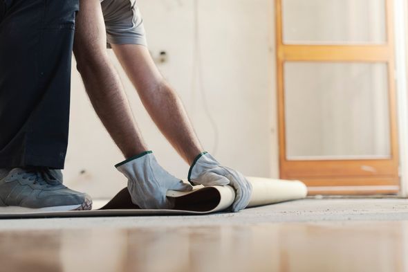 A man is rolling a piece of carpet on the floor.