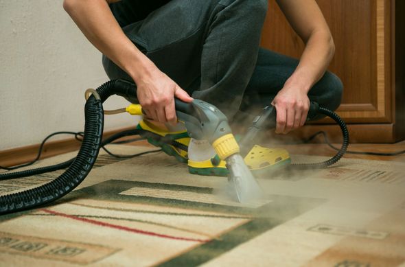 A person is cleaning a rug with a vacuum cleaner.
