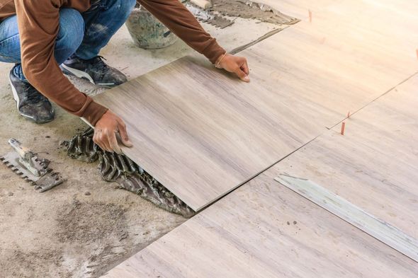 A man is laying tiles on the floor with a trowel.