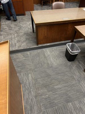A person is standing in a room with a desk and a trash can.
