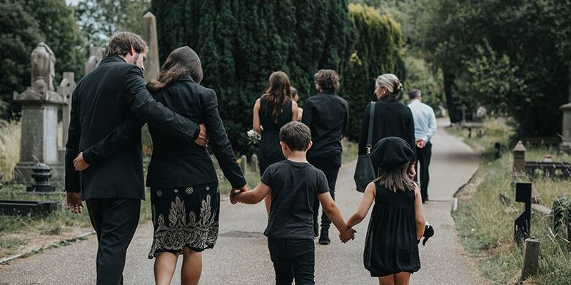a group of people are walking down a path in a cemetery holding hands .