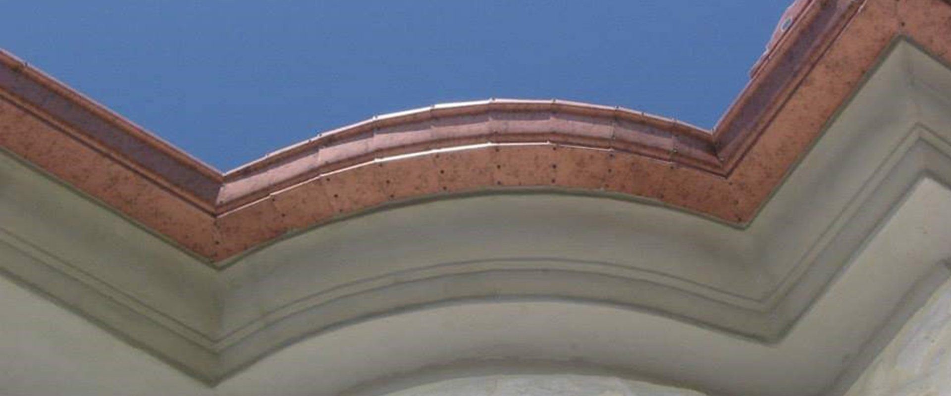 Un tetto con una grondaia di rame e un cielo azzurro sullo sfondo.