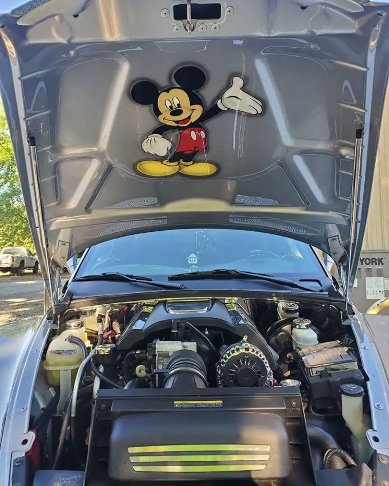 Silver car engine bay with Mickey Mouse decal on the hood.