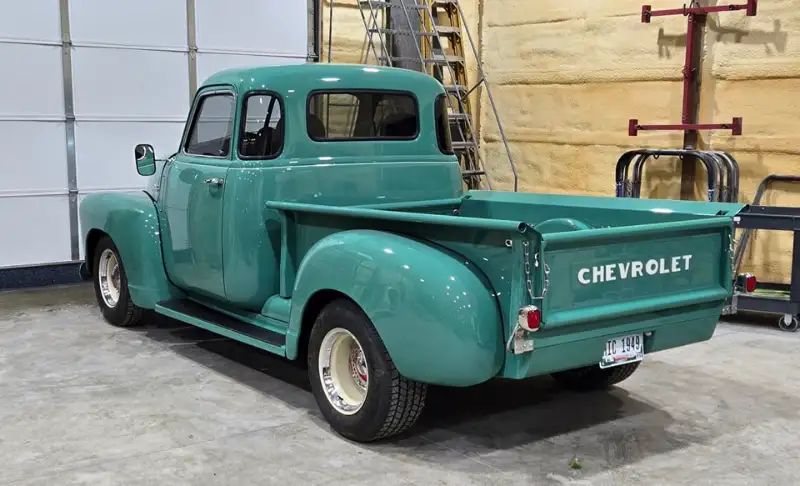 Green vintage Chevrolet pickup truck in a garage.