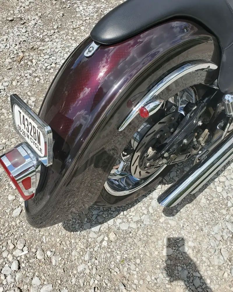 Motorcycle rear fender, dark red-purple, chrome accents, rear tire visible, license plate and tail light.